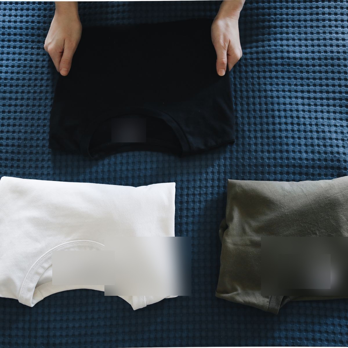 Three folded crewneck tees in black, white, and olive