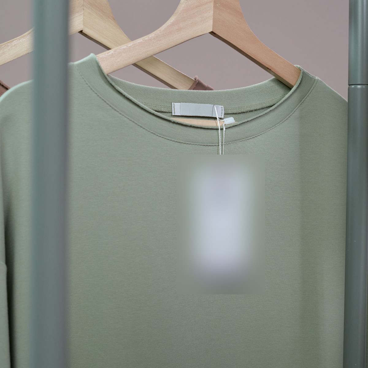 A sage green cotton tee on a wooden hanger